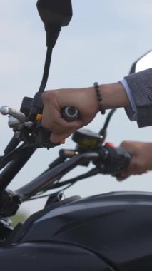 Beyaz bir adam elektrikli motosiklet kullanıyor. Erkek ellerinin direksiyona yakın plan çekimi. Dikey video