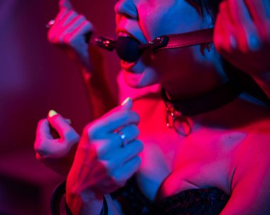 Bir adam, yatak odasında pembe mavi neon ışıklı bir kadının ağzını tıkar. BDSM konsepti