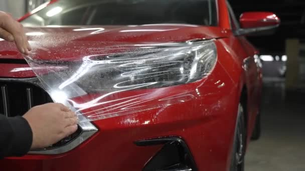 主人把乙烯薄膜涂在一辆红色汽车的前灯上 — 图库视频影像