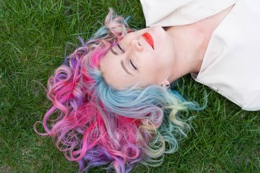 Kafkasyalı kadının yeşil çimlerin üzerinde uzanan çok renkli saçları var.