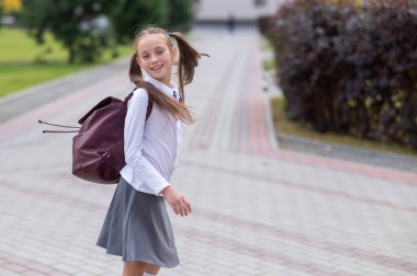 Üniformalı ve sırt çantalı mutlu bir beyaz kız okuldan sonra dışarı çıkıyor.