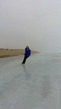 Mavi kazaklı beyaz kadın donmuş bir gölde paten kayıyor. Artistik patinajcı programı gerçekleştirir