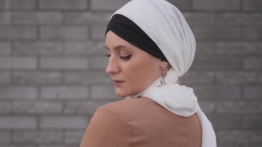 Mavi gözlü genç bir kadının portresi gri tuğla bir duvara karşı tesettürlü. Müslüman bir kadın dönüp kameraya bakar.