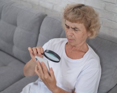 Miyoplu yaşlı, beyaz bir kadın ve akıllı telefondan bir büyüteçle mesaj okumaya çalışıyor.