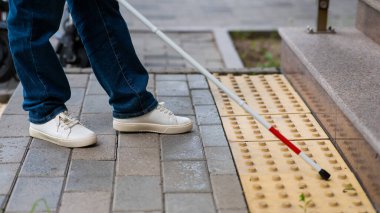 Kadın ayağı, baston ve dokunsal fayansların yakın çekimi. Kör kadın baston kullanarak merdivenleri çıkıyor.