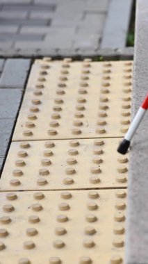 Kadın ayağı, baston ve dokunsal fayansların yakın çekimi. Kör kadın baston kullanarak merdivenlerden iniyor. Dikey video