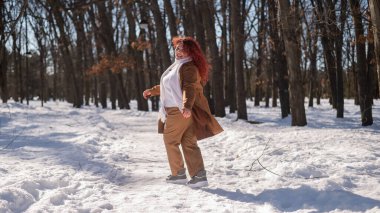 Portrait of an excited red-haired curly fat woman in the park in winter