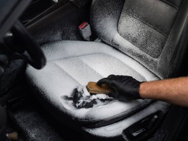 Siyah deri koltuğu fırça ve köpükle temizleyen adam.