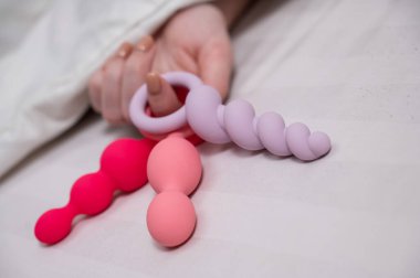 Yatakta yatarken elinde üç farklı anal boncuk tutan kadın.