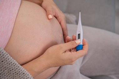 Hamile kadın koltukta otururken sıcaklık ölçer. Karnını kapat.