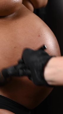 Usta, hamile bir kadının tenindeki fırçayla anında bronzlaşır. Karnına yakın çekim yap. Dikey fotoğraf