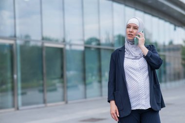 Başörtülü ve takım elbiseli iş kadını akıllı telefondan konuşuyor.