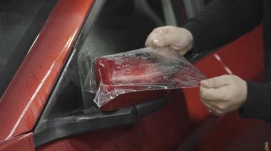 Usta bir arabanın dikiz aynasına vinil film uyguluyor.