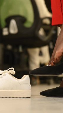 Afrikalı bir kadın ofiste yüksek topukludan spor ayakkabısına dönüşüyor. Yorgun bacaklar. Dikey video