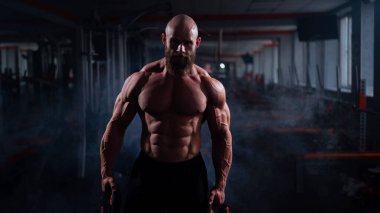 Ağırlık plakası tutan kaslı, kel, üstsüz bir adam. Vücut geliştiren biri spor salonunda vücudunu gösterir.