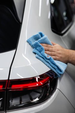 Bir tamirci mikrofiber bezle beyaz bir arabanın vücudunu siler.