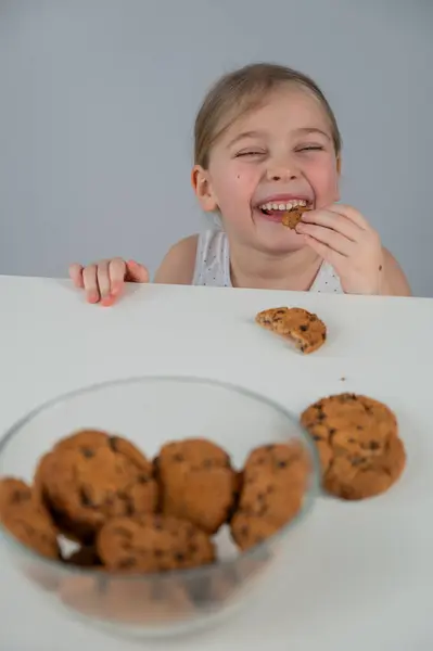 A little girl steals cookies from the table. Vertical photo