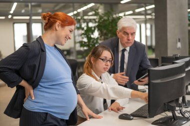 An elderly man, a Caucasian woman and a pregnant woman are discussing work issues at the computer clipart