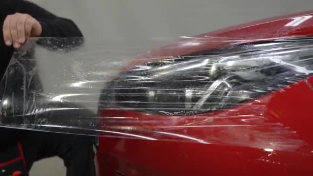 主人把乙烯薄膜涂在一辆红色汽车的前灯上 — 图库视频影像