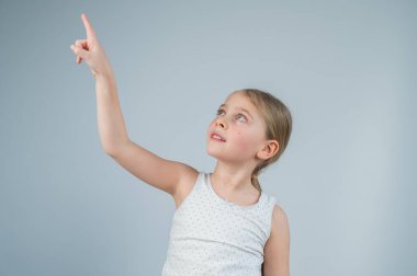 Küçük beyaz kız eğleniyor ve beyaz arka planda parmakla gösteriyor.