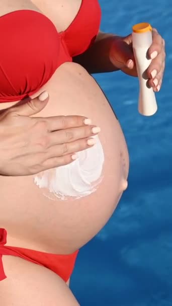 孕妇穿着红色比基尼晒日光浴时的腹部特写 准妈妈涂防晒霜 垂直录像 — 图库视频影像