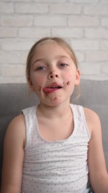 Kanepede çikolatayla kaplanmış kurabiye yiyen tatlı küçük kız. Dikey video