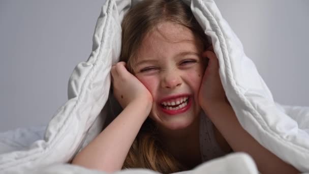 Портрет Милої Маленької Дівчинки Робить Обличчя Ховається Під Ковдрою — стокове відео
