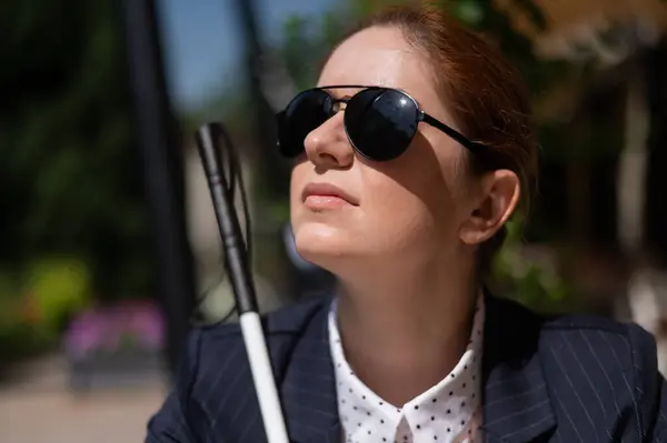 A blind woman in a business suit is sitting in an outdoor cafe
