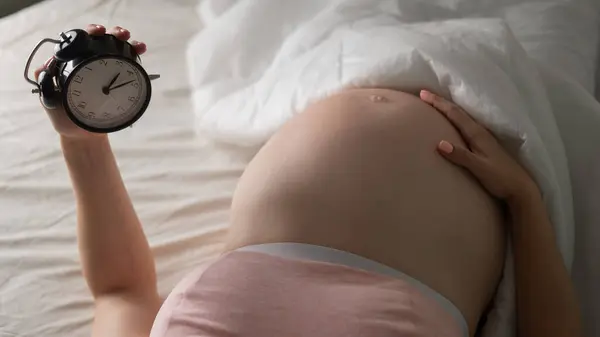 Μια Έγκυος Ξαπλώνει Στο Κρεβάτι Και Κρατάει Ένα Ξυπνητήρι Κλείσε — Φωτογραφία Αρχείου