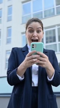 Dikey video 360 derece. Kafkasyalı iş kadını akıllı telefona bakıyor ve dışarıda gülmeye başlıyor.