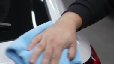 Bir tamirci mikrofiber bezle beyaz bir arabanın vücudunu siler.