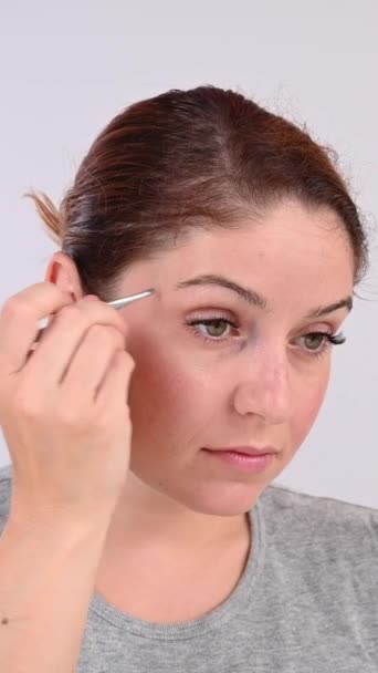 白人女性は鏡を見つめ 眉毛をツイッターで修正しています バーティカルビデオ — ストック動画