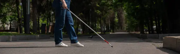 Blind woman crosses the street with the help of a tactile cane. Wide screen