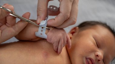 Bir kadın, yeni doğmuş bir çocuğun elini tırnak makası ile keser. Ellerin yakın çekimi