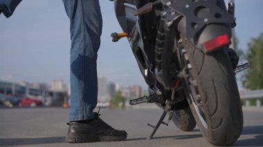 Adamın biri elektrikli motosiklete biniyor, amuda kalkıyor ve uzaklaşıyor.