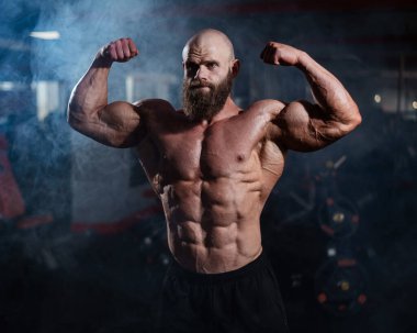 Tişörtsüz poz veren kaslı kel adam. Vücut geliştirici spor salonunda vücudunu gösteriyor.