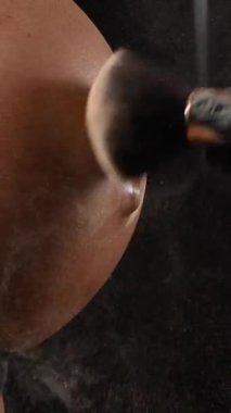 Usta, bronzlaştırma işleminden sonra hamile bir kadının cildine ışıltıyla pudra sürer. Karnına yakın çekim yap. Dikey fotoğraf