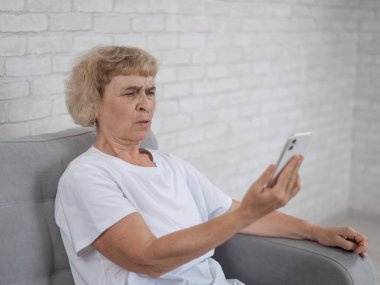 Yaşlı beyaz bir kadın miyopluktan muzdarip ve kolları açık bir şekilde akıllı telefondan mesaj okumaya çalışıyor.