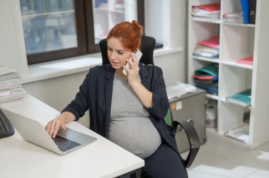 Ofiste cep telefonu kullanan hamile kadın.
