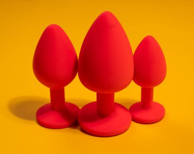 Three size silicone red butt plugs on an orange background