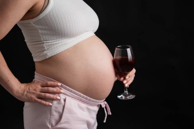 Kanepede otururken elinde bir bardak kırmızı şarap tutan hamile bir kadının göbeğine yakın plan.
