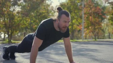 Uzun saçlı sakallı adam spor sahasında şınav çekiyor.