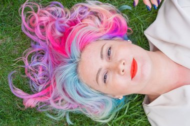 Kafkasyalı kadının yeşil çimlerin üzerinde uzanan çok renkli saçları var.