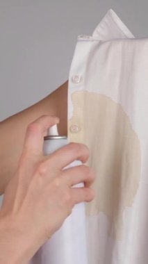 Kadın, ofis beyaz gömleği için kahve lekeli leke çıkarıcı sprey kullanıyor. Kız bluzunda çamaşır suyu kullanıyor. Dikey video