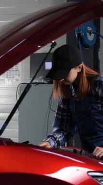 Kadın oto tamircisi dizüstü bilgisayar kullanarak motor kontrolü yapıyor. Dikey video