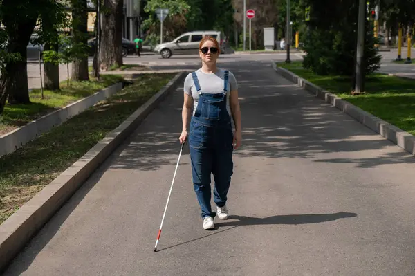 Blind pregnant woman walking down the street with a cane