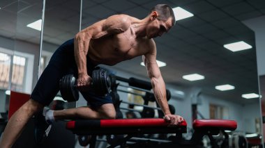 Gömleksiz bir adam spor salonunda dambıl sırasına dizer.
