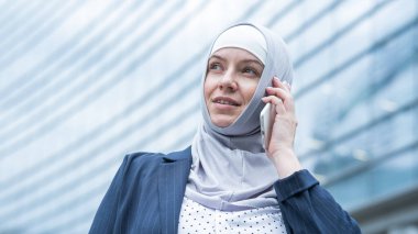 Başörtülü ve takım elbiseli iş kadını akıllı telefondan konuşuyor.