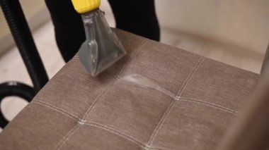 Kadın, elektrikli süpürge ve fırça kullanarak kumaş sandalyesini temizliyor.