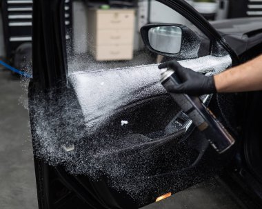 Adamın biri arabanın içini köpükle temizliyor.